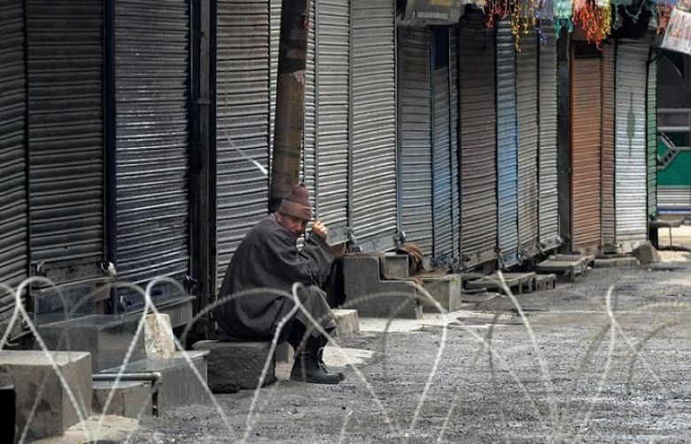 A Kashmiri sits in front of shuttered shops behind a barbed wire roadblock during a curfew in Srinagar on February 9, 2014.