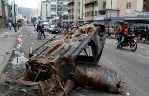 People walk close to a destroyed car in a street, after a protest in Caracas 