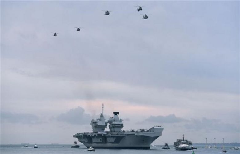 Wildcat and Merlin helicopters fly above the 65,000-tonne British aircraft carrier HMS Queen Elizabeth as tug boats maneuver it into Portsmouth Harbor in Portsmouth, southern England, August 16, 2017.