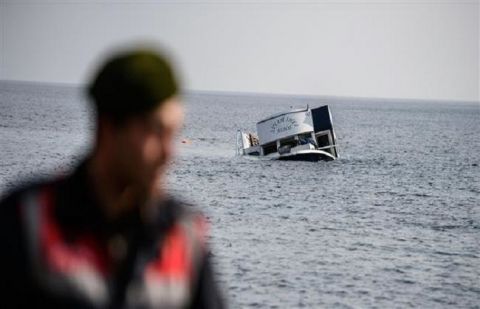 A sinking boat is seen behind a Turkish gendarme off the coast of Canakkale's Bademli district on January 30, 2016.