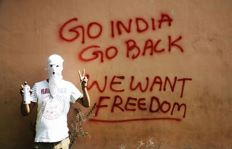 A masked Kashmiri protester shows the victory sign after drawing graffiti on the wall of a building in Srinagar, Sept 27, 2016.