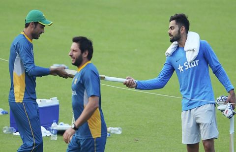 India's Virat Kohli presents a cricket bat to Pakistan's Mohammad Amir as Pakistan's captain Shahid Afridi walks past during a training session at The Eden Gardens in Kolkata. 