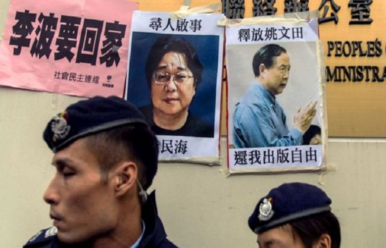Police walk past missing person notices for Gui Minhai, posted on the Chinese Liaison Office in Hong Kong