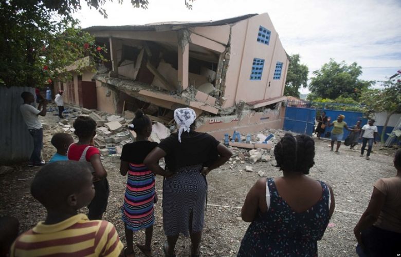 Residents stand looking at a collapsed school damaged by a magnitude 5.9 earthquake the night before, in Gros Morne, Haiti, Oct. 7, 2018.